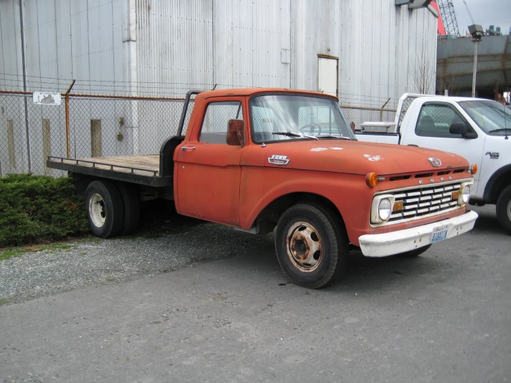 an orange old pick up truck parked next to other trucks