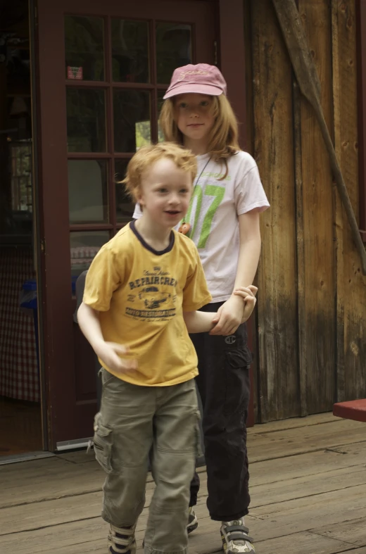 a young woman in a hat and yellow t - shirt is talking to a child on skateboards