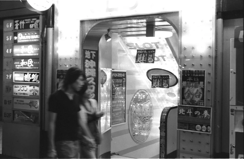 two people walking past an arcade machine, a ticket stand and a movie poster