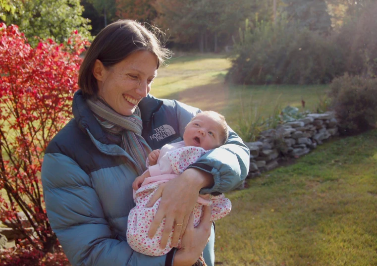 a woman is holding a baby who is wrapped in a coat