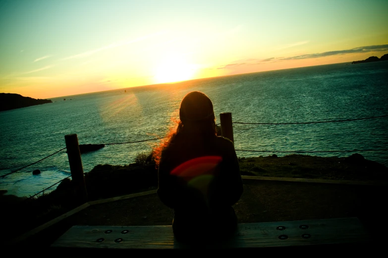 a woman looks at a bright sunset over the ocean