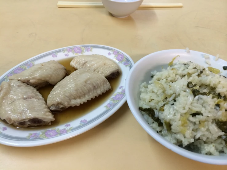 a couple plates with chicken wings and rice with chop sticks next to it