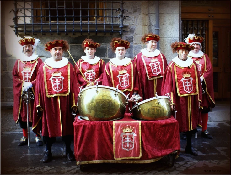 men dressed in red clothing are standing behind a golden instrument