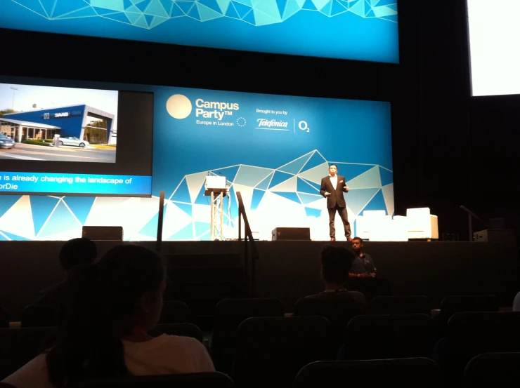 a man giving a speech on stage with a big screen in the background