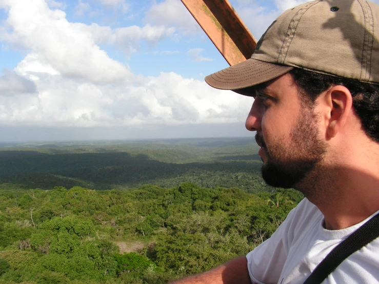 man looking out over a green mountain area with white clouds