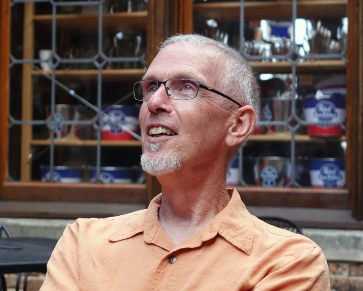 an older man wearing glasses sits at a table and smiles