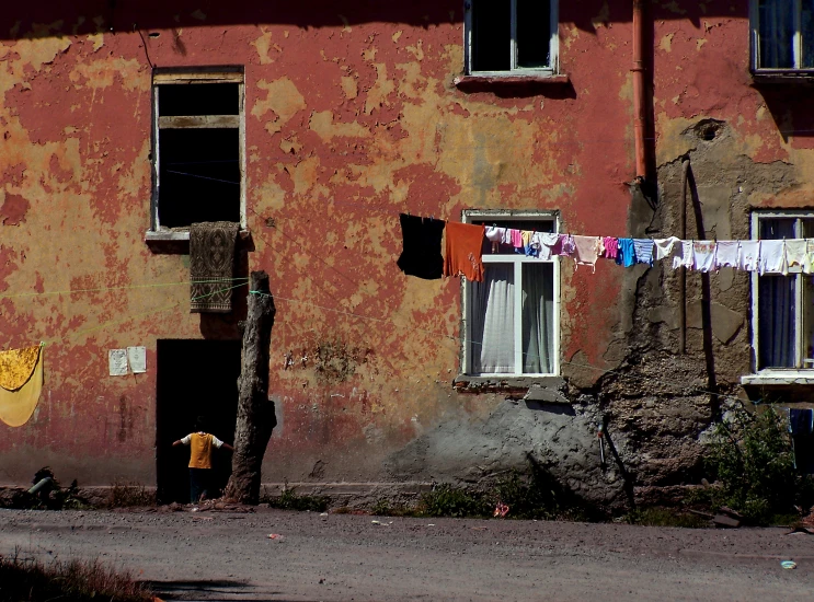 a person sitting on a bench next to an orange building with clothes hanging out