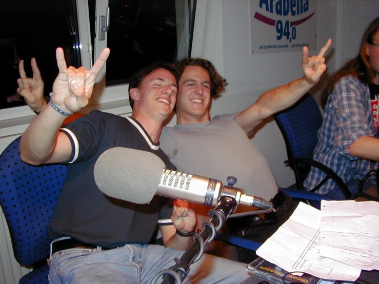 two men sitting in chairs while one holds up his microphone