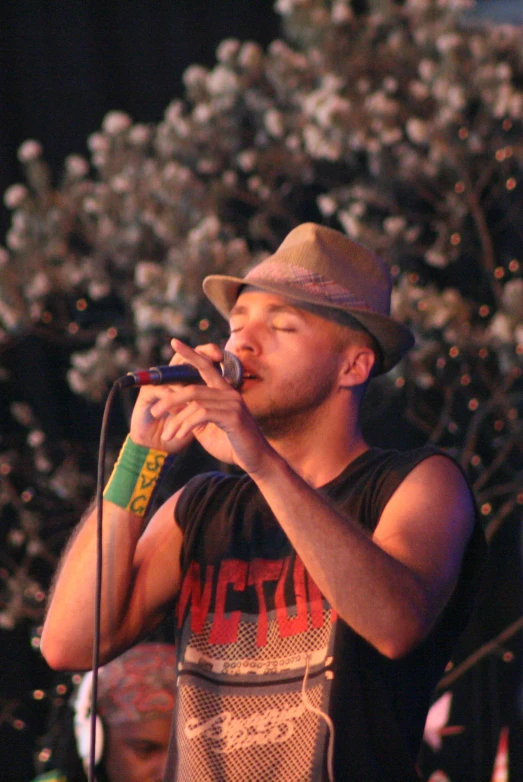 a man in a fedora on stage with a microphone