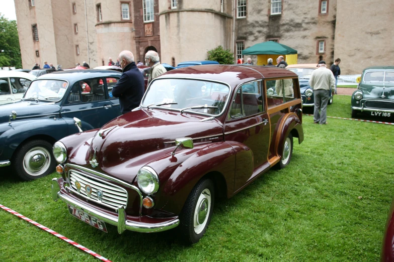 an old maroon car parked on a lush green field