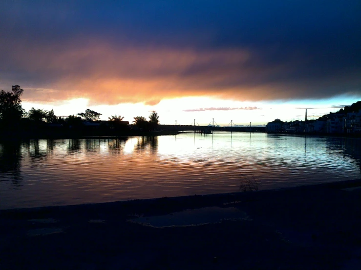 a lake during a sunset with a dark sky in the background