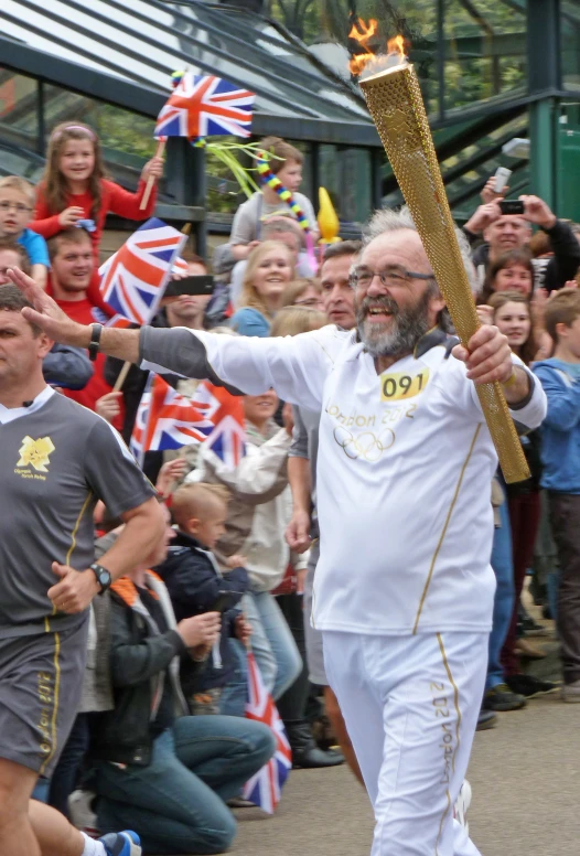 an old man in white holds up his baton with fire as he leads his team