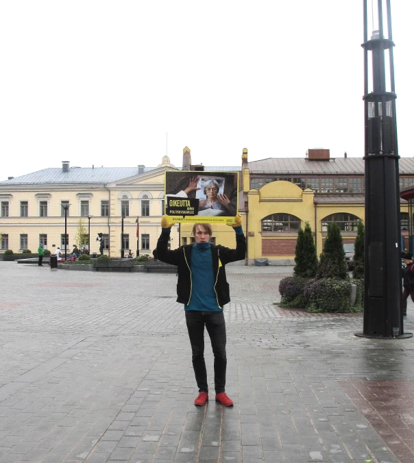 man in blue shirt holding up sign with yellow building in background