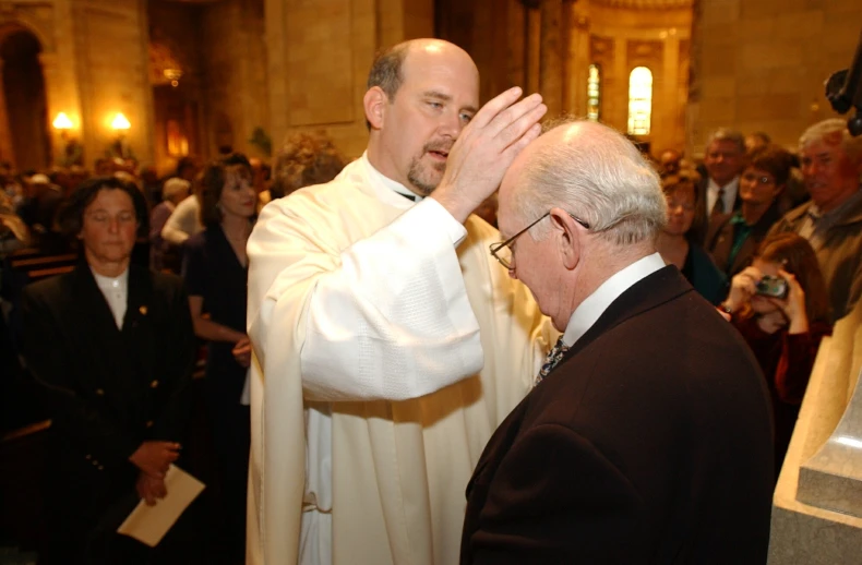 the priest is holding his hands up and looking at the camera man's face