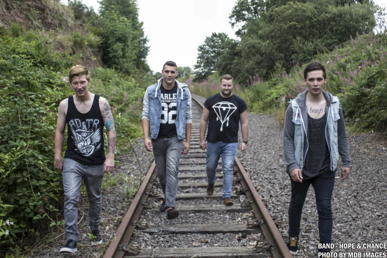 a group of young men walk on railroad tracks