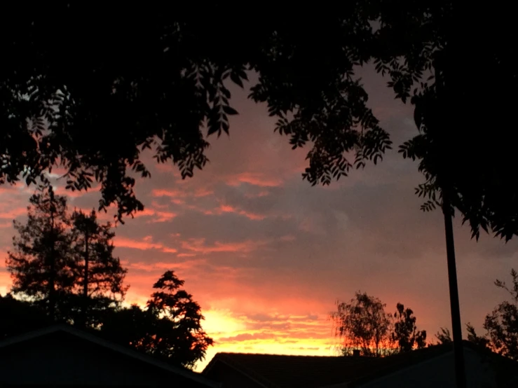 a sunset over trees and a house with a red and orange sky in the background