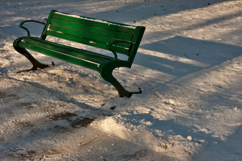 the green bench is covered in snow at the park