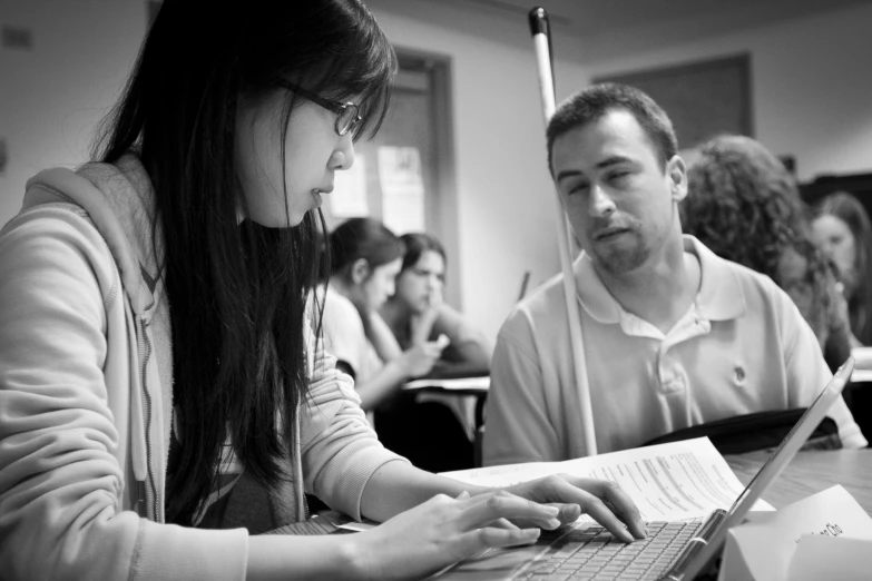 two people looking at a book and one using a laptop