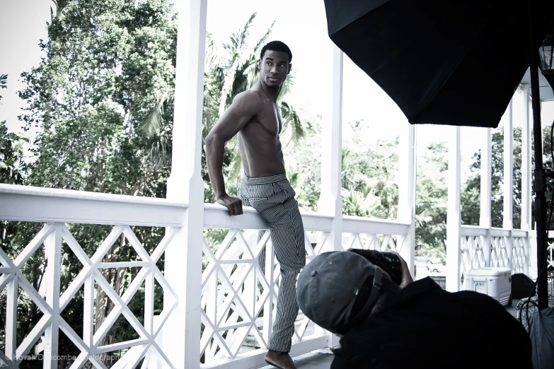 a man in pajamas posing on a porch with an umbrella over him