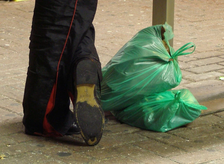 a person in black pants and brown sneakers next to a green bag