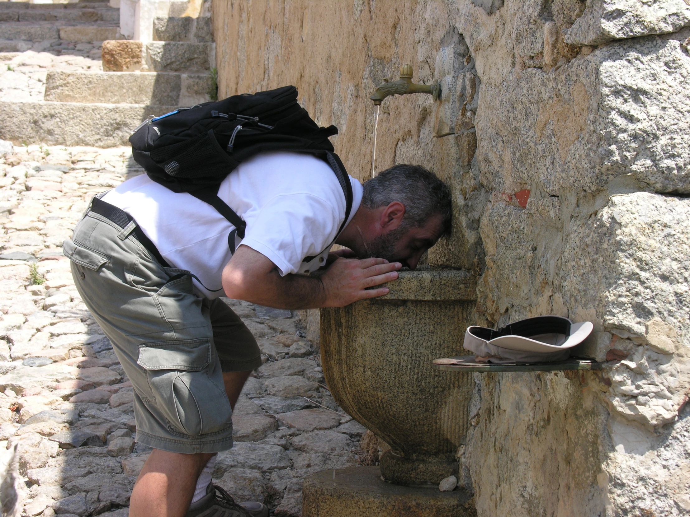 a man wearing shorts and a white shirt is drinking from a large outdoor urn