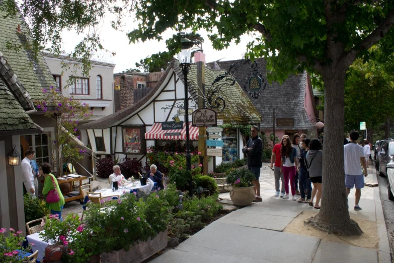 people walking by a store on a sidewalk with lots of potted plants