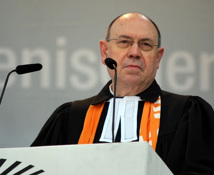 a priest wearing an orange and white robe standing at the podium