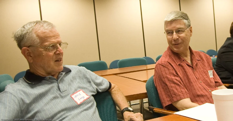 an older man sitting next to another older man at a conference room