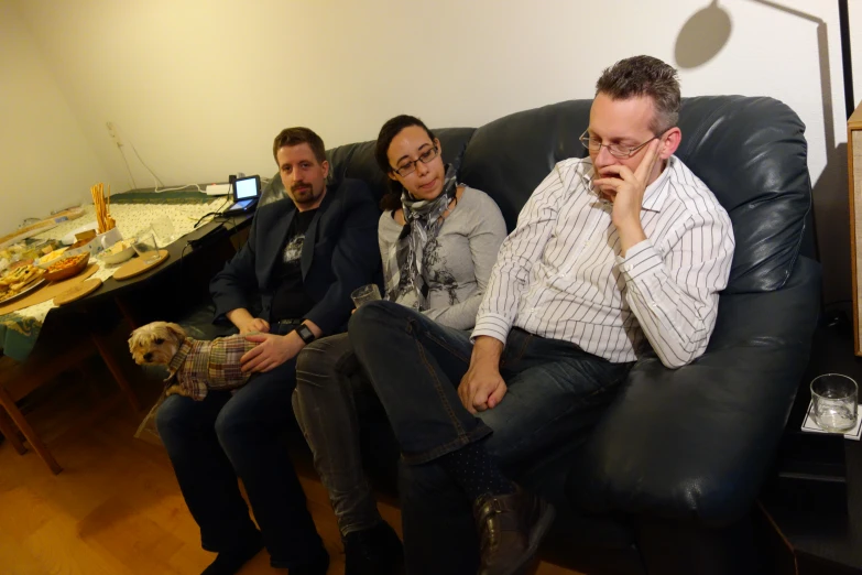 three men sitting on a black leather couch