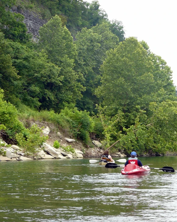 people riding kayaks down a river with rocky bank