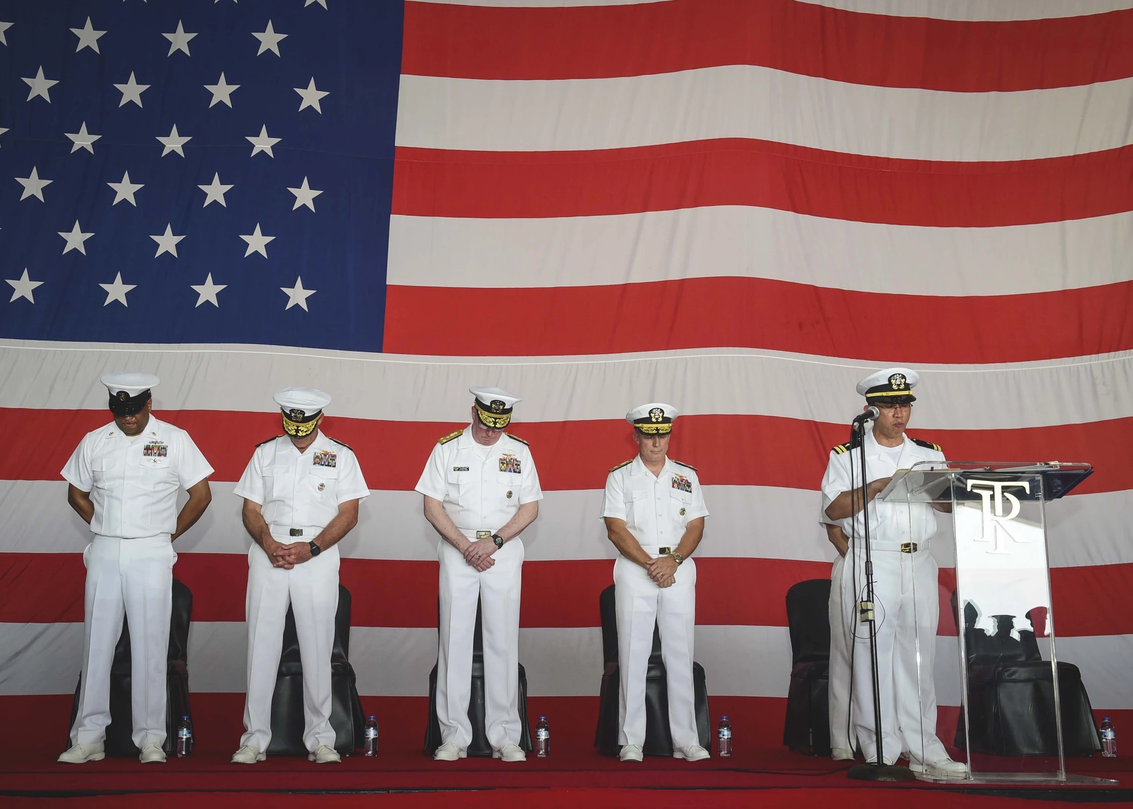 a row of men wearing navy uniforms stand in front of an american flag