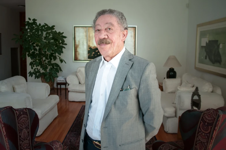 an older man wearing a suit standing in front of couches