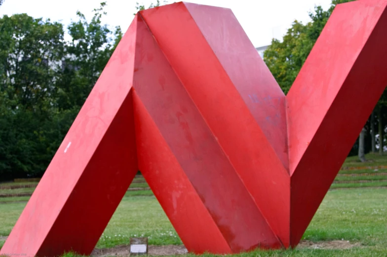 a red sculpture sits in a field behind a forest