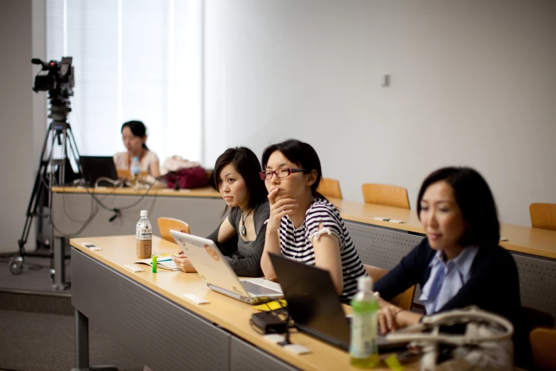 four people sit at desks in a classroom