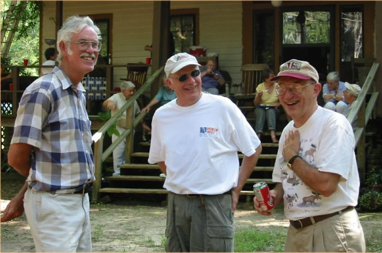 three men pose for a picture in front of a house