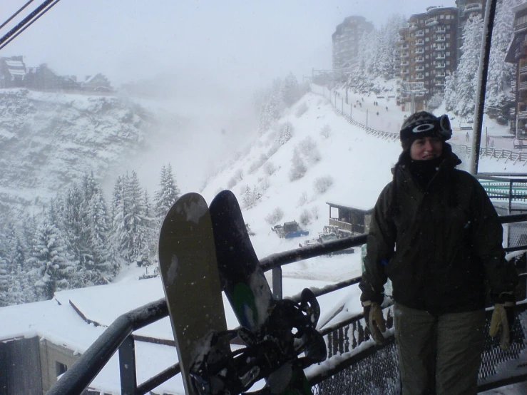 a man in green jacket holding snow board standing by railing