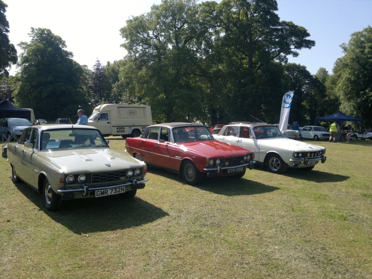 four different old cars on a field near trees