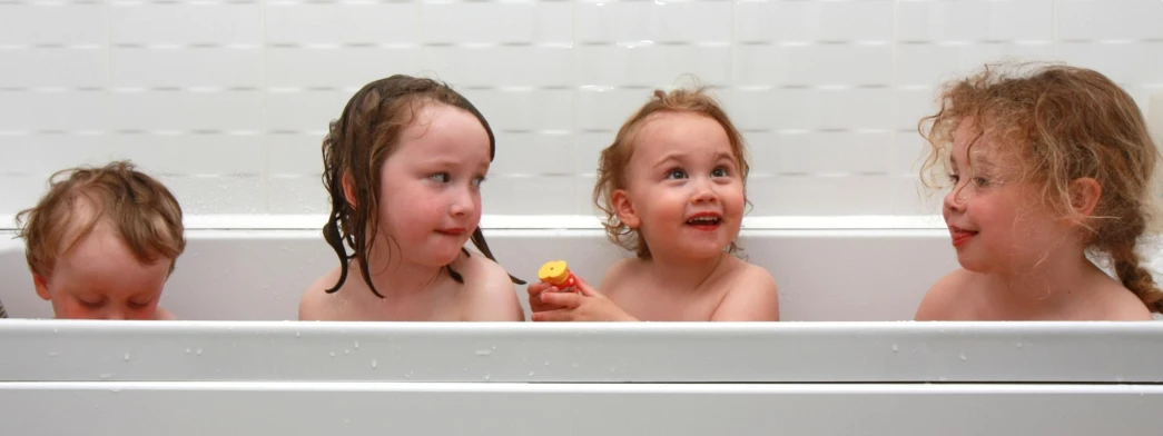 three children are sitting in the bath tub and having a snack