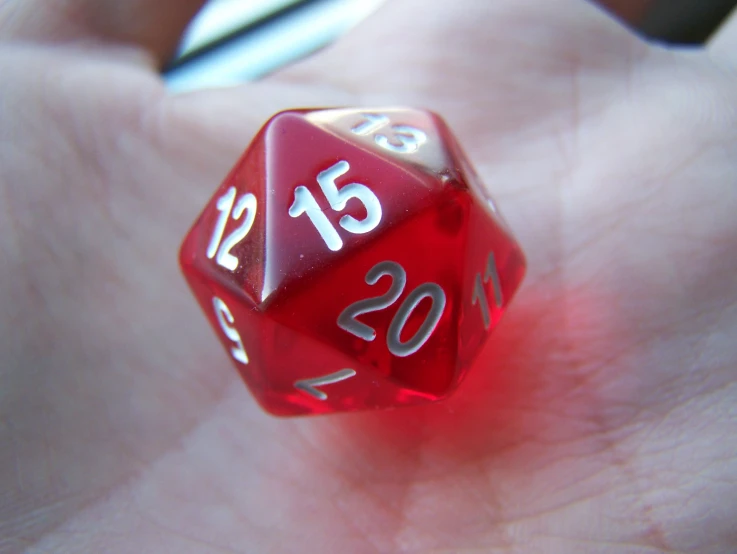 a red d20 dice with numbers and symbols being held in palm