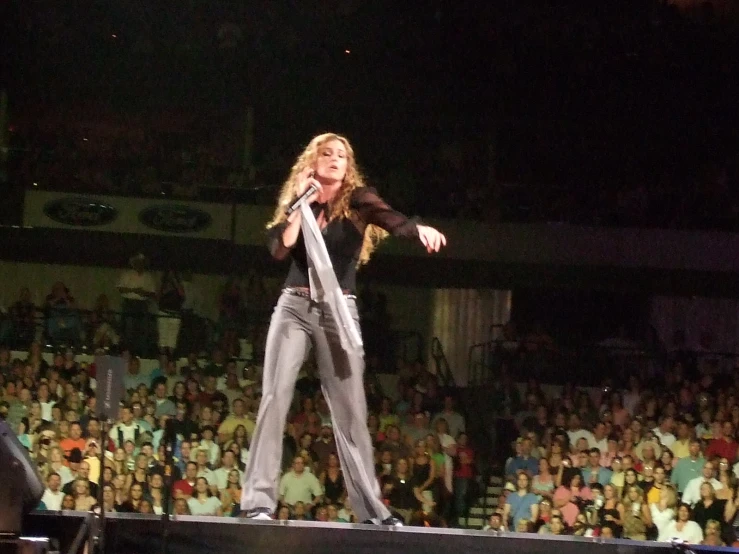 a woman is standing on a stage with her arms outstretched, and a crowd watching