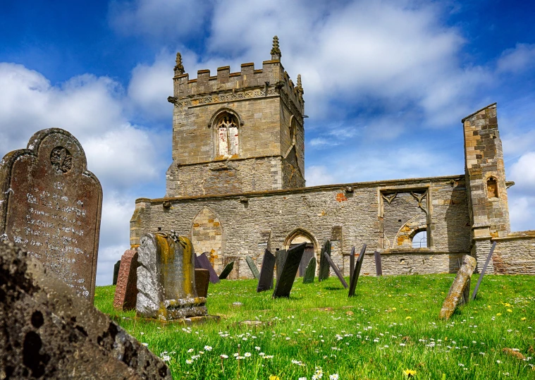 an old stone church with a steeple standing in the middle of a grass field