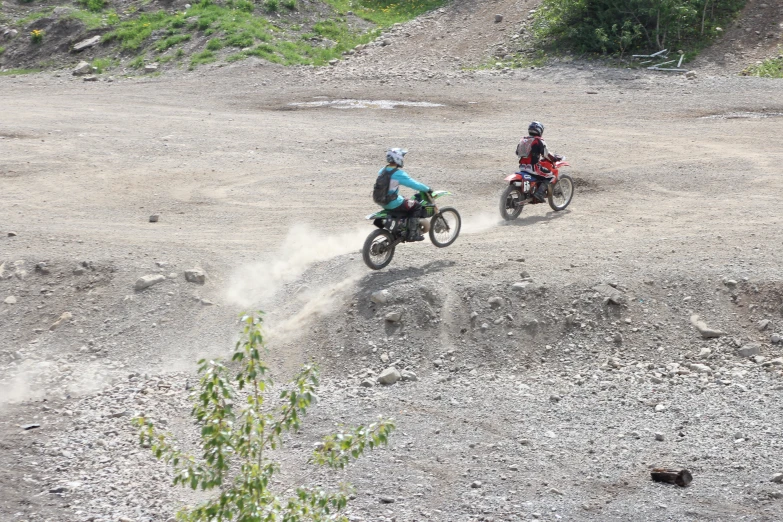 two people ride motorcycles on an open gravel ground