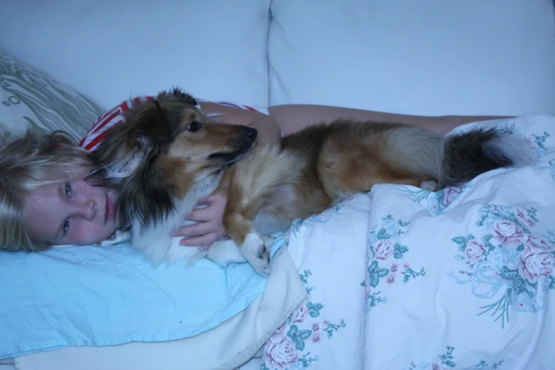 a young woman holding her small dog lying on a bed