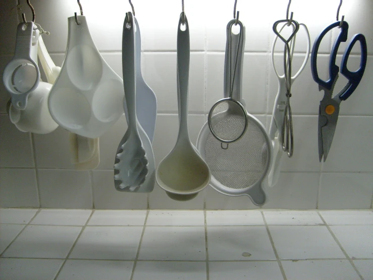 many utensils hanging in a rack on a tiled wall