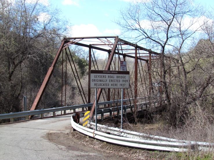 a very tall rusty metal bridge near some trees