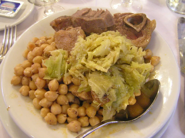 a plate full of beans and meat next to silverware on a table
