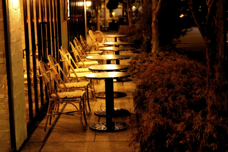 tables, chairs, and bench sitting along the street at night