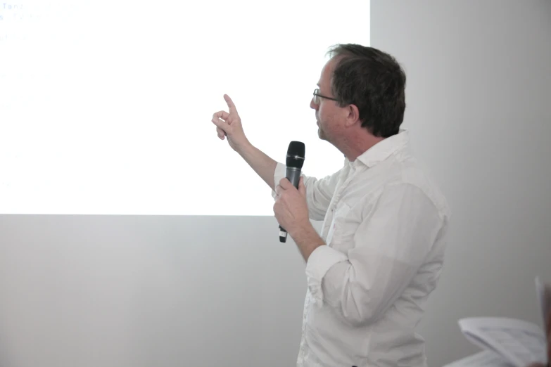 a man wearing glasses and white shirt talking on the screen with hand out