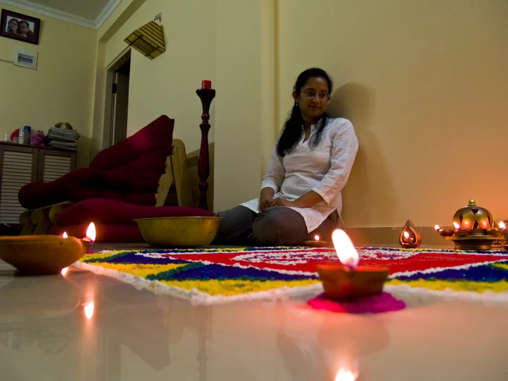 a woman sitting on a mat of some sort with candles surrounding her