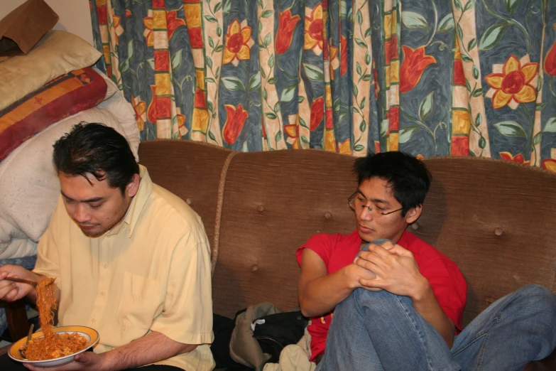 two men sitting on a couch and eating